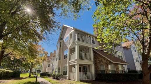 Three-story condo building with white balconies under big trees