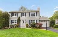 Gray two-story Colonial with black shutters and a green front lawn