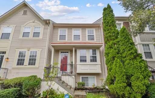 Beige townhome with a red front door and tall evergreens